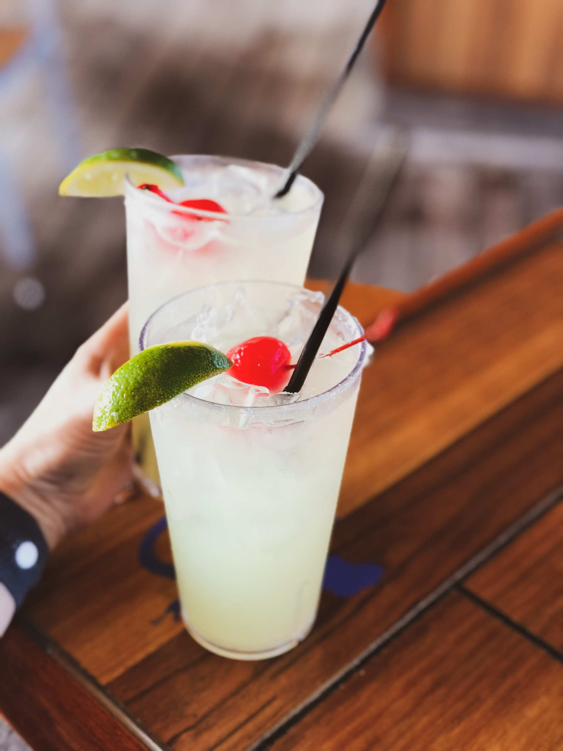Two glasses of Almendra Colada on a wood table, with a hand reaching for one
