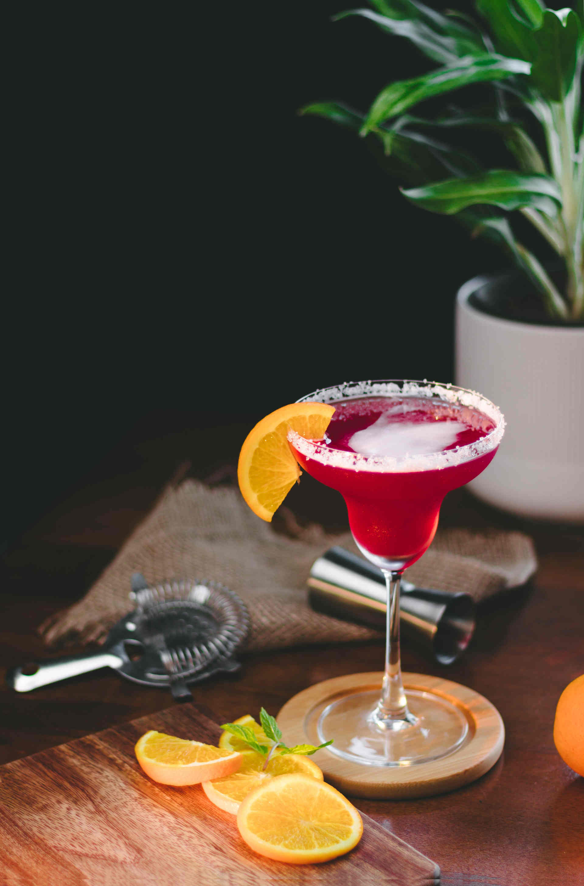 A granata cocktail sitting on a desk with lemon slices and cocktail tools 