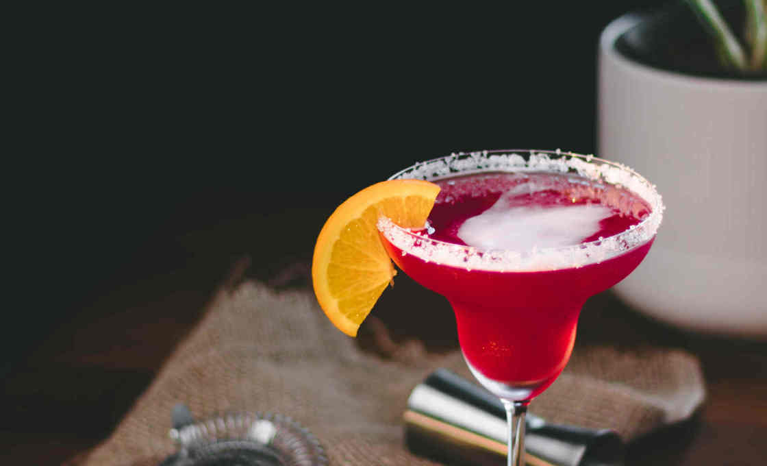 A granata cocktail sitting on a desk with lemon slices and cocktail tools 