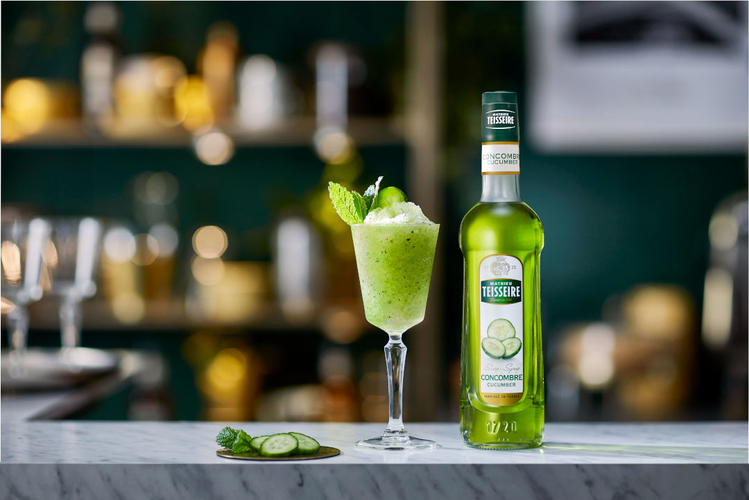 Bottle of Mathieu Teisseire cucumber syrup with a cocktail and garnish