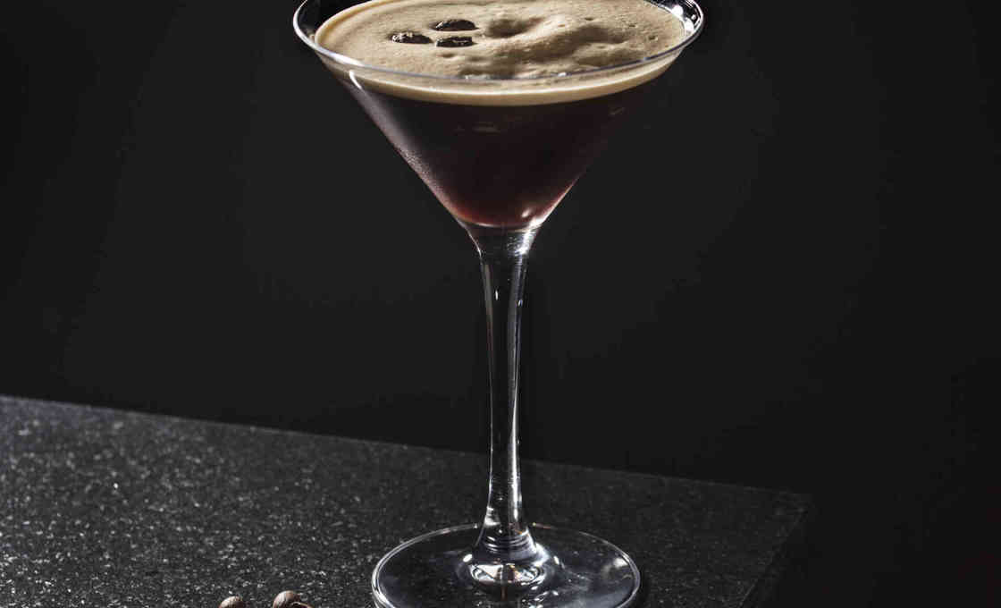 martini glass of Tiramisu Creamy Martini on the edge of a stone surface with loose coffee beans