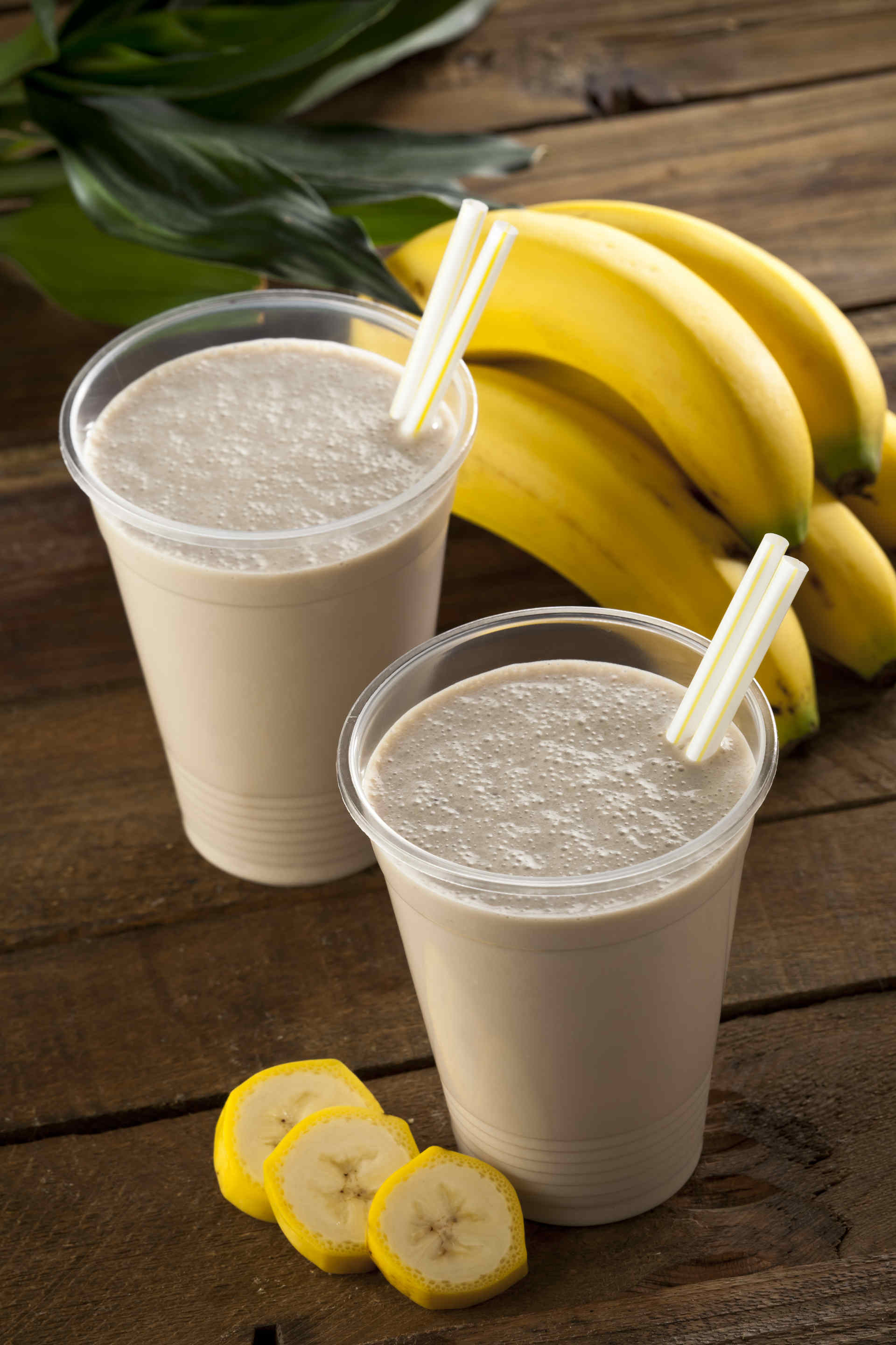 Two choco-banana milkshakes on a  table with a bunch of bananas