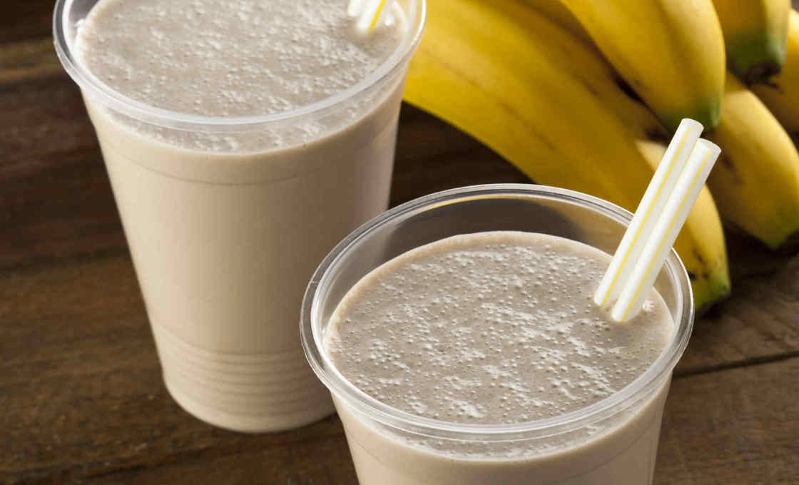 Two choco-banana milkshakes on a  table with a bunch of bananas