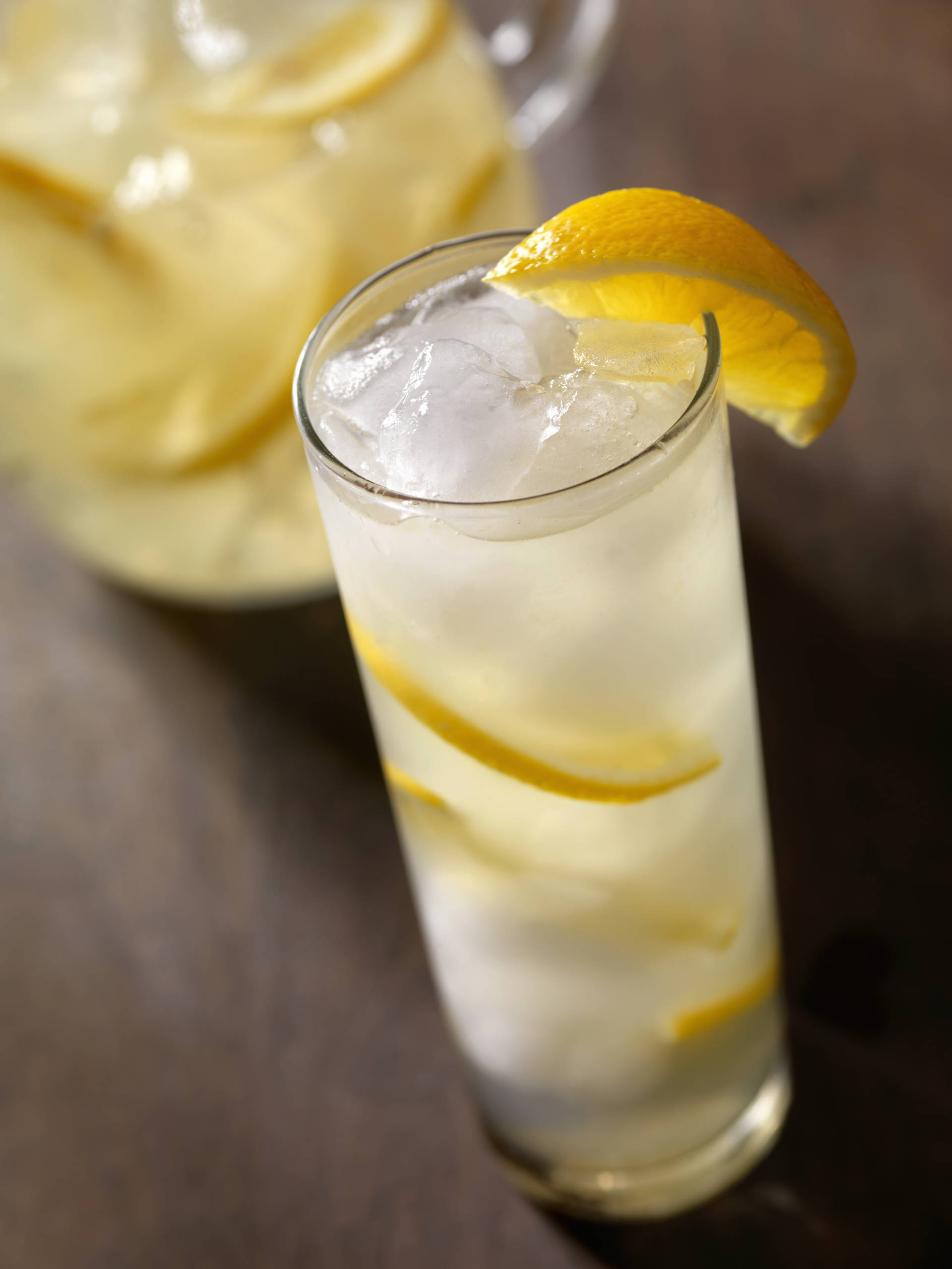 A jug and glass of lemonade with sliced lemons on a wooden table