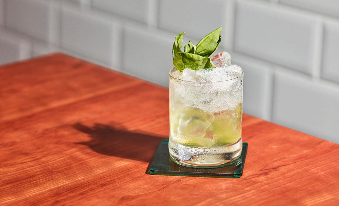 Glass of Botanist Sparkler on a wooden table against a tiled wall