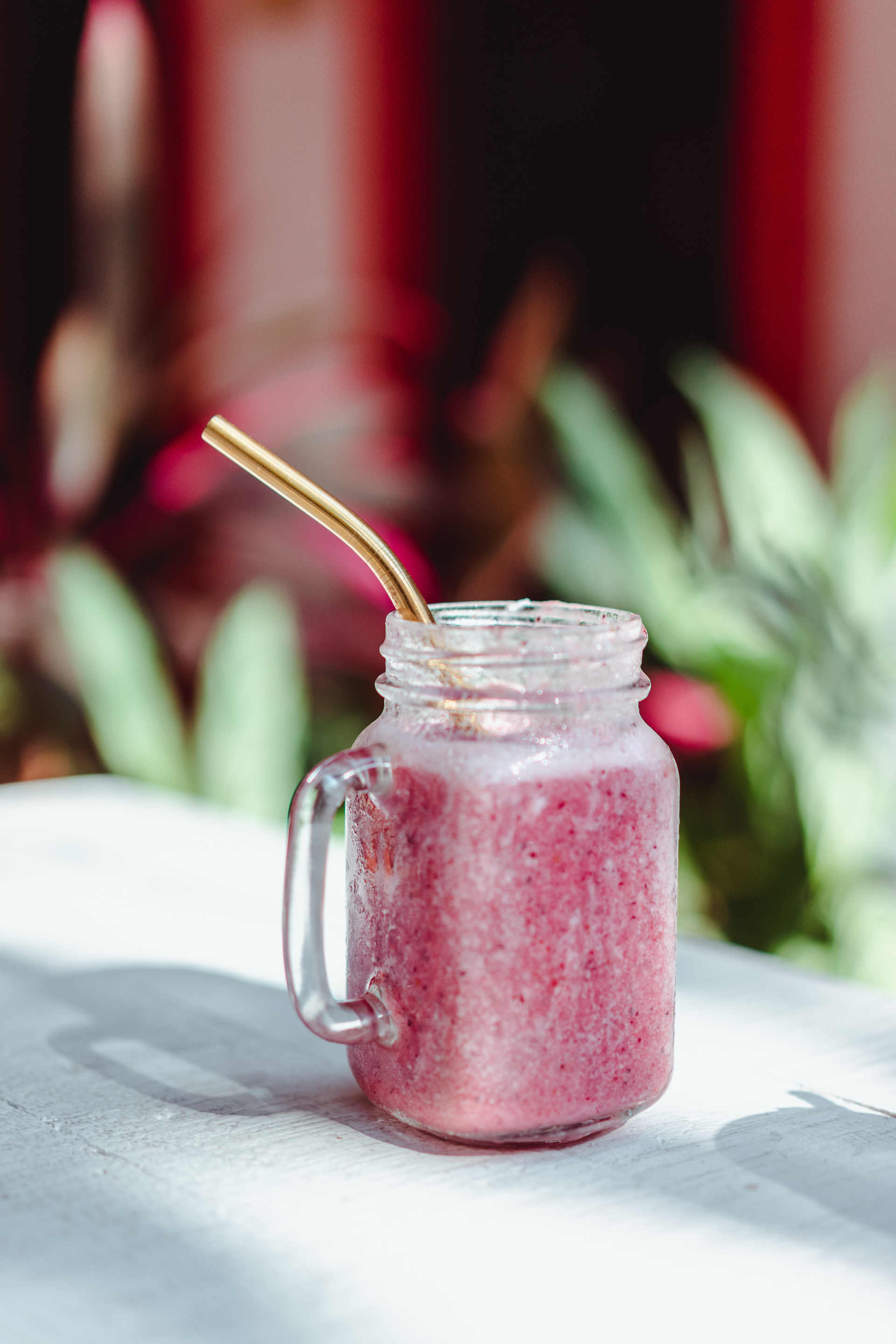 A mug of Boozy Strawberry milk on a table with plants in the background