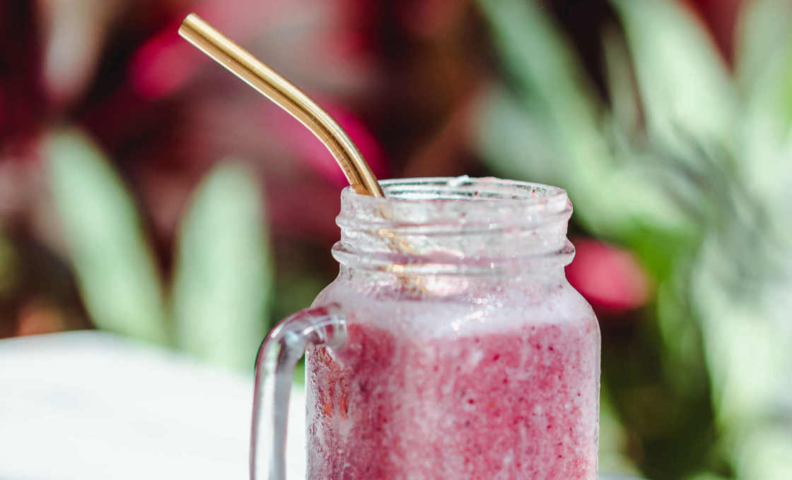 A mug of Boozy Strawberry milk on a table with plants in the background