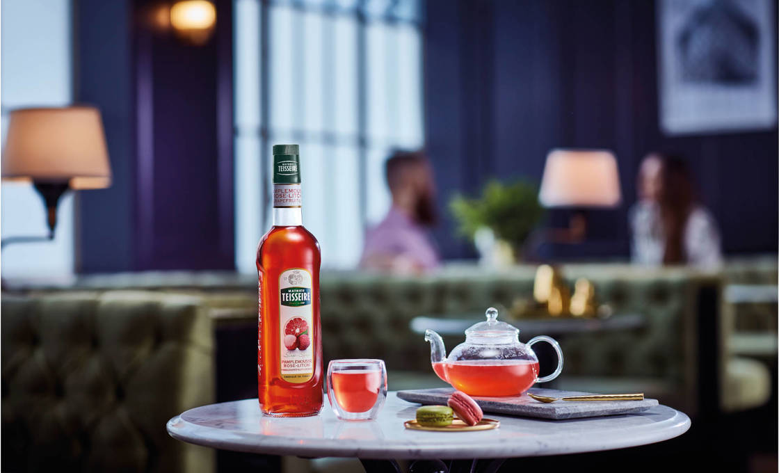 A glass of Asian spirit with glass teapot, macarons, and a bottle of Mathieu Teisseire Pink Grapefruit Lychee  syrup