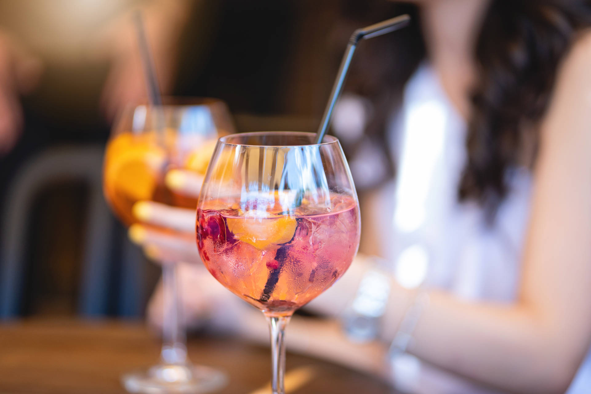 Glass of Cotton Candy Spritz with a woman holding a cocktail in the background