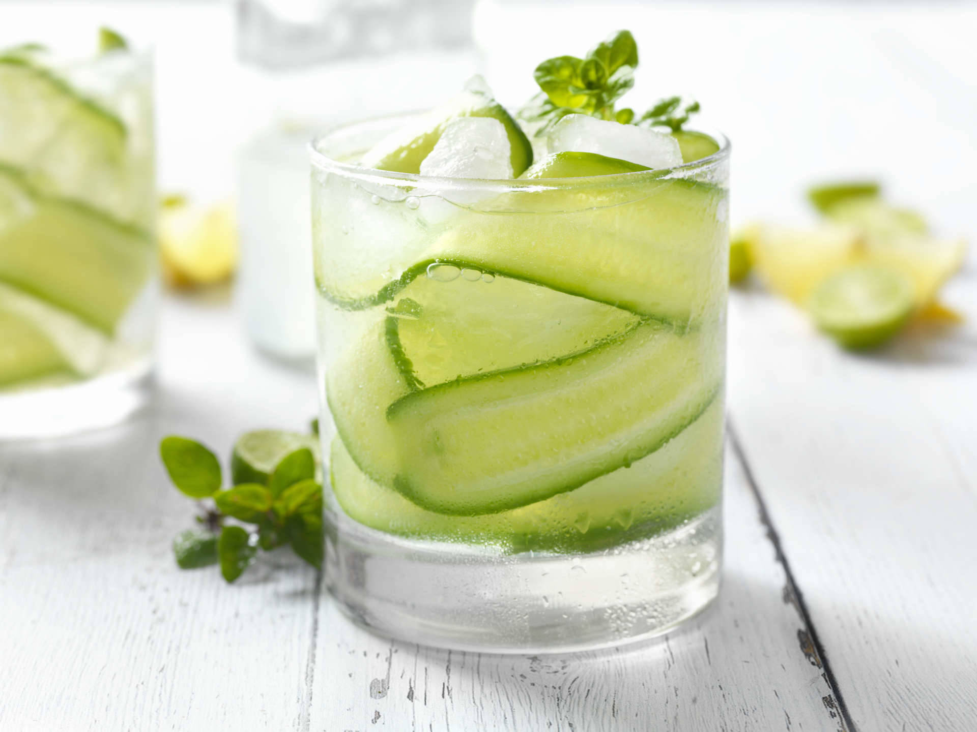 A glass of cucumber and basil soda on a white wooden table